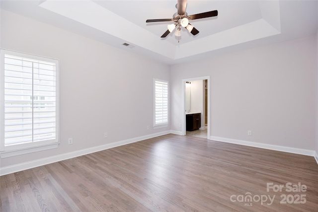 empty room with a raised ceiling, a ceiling fan, light wood-style flooring, and baseboards
