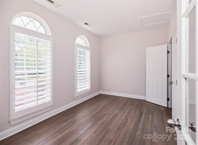 unfurnished room with dark wood finished floors, attic access, and baseboards