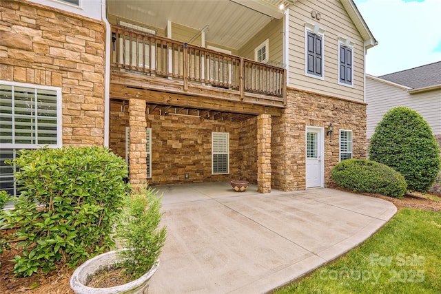 back of house featuring stone siding, a patio area, and a balcony
