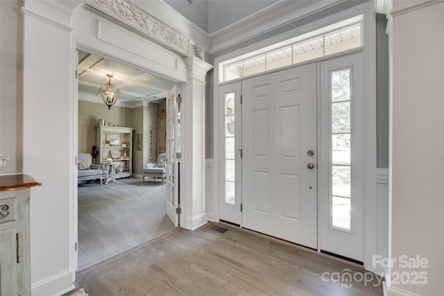 carpeted entryway with crown molding, decorative columns, wood finished floors, baseboards, and a notable chandelier