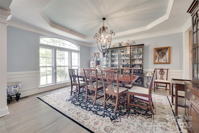 dining space with crown molding, wainscoting, a tray ceiling, light wood-style flooring, and a notable chandelier