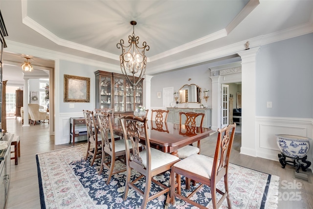 dining space with a wainscoted wall, ornamental molding, light wood-style flooring, and a notable chandelier