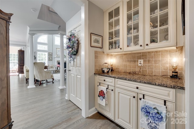 bar with ornate columns, decorative backsplash, light wood-style floors, and lofted ceiling