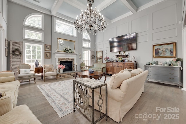 living room with a fireplace, light wood-style floors, a high ceiling, coffered ceiling, and a notable chandelier