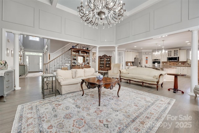 living area featuring stairs, ornate columns, a chandelier, and a towering ceiling