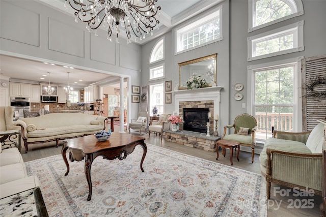 living room featuring wood finished floors, a high ceiling, a stone fireplace, and a notable chandelier