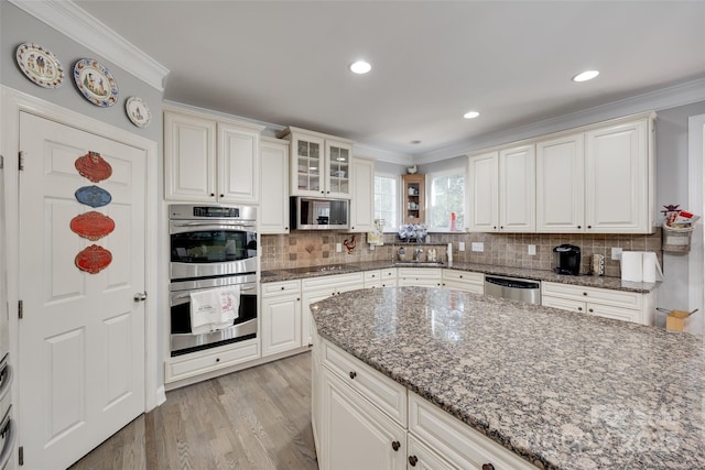 kitchen with crown molding, appliances with stainless steel finishes, light wood finished floors, dark stone countertops, and tasteful backsplash