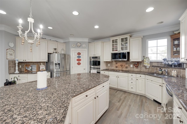 kitchen featuring appliances with stainless steel finishes, a sink, decorative backsplash, ornamental molding, and glass insert cabinets
