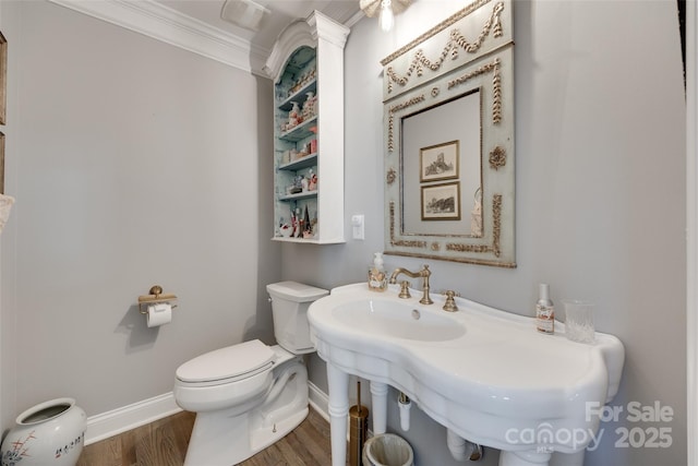half bath featuring crown molding, wood finished floors, toilet, baseboards, and a sink