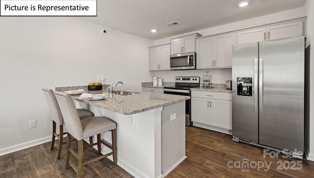 kitchen with dark wood-style floors, light stone countertops, a sink, a kitchen bar, and appliances with stainless steel finishes