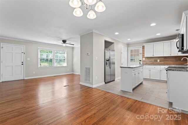 kitchen with visible vents, a center island, stainless steel fridge with ice dispenser, ceiling fan with notable chandelier, and ornamental molding
