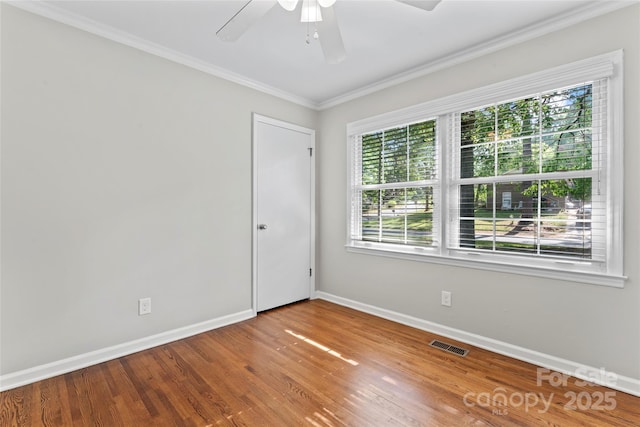 spare room featuring ceiling fan, baseboards, wood finished floors, visible vents, and ornamental molding