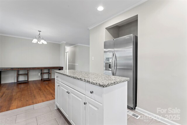 kitchen featuring stainless steel refrigerator with ice dispenser, crown molding, light stone countertops, white cabinets, and a chandelier