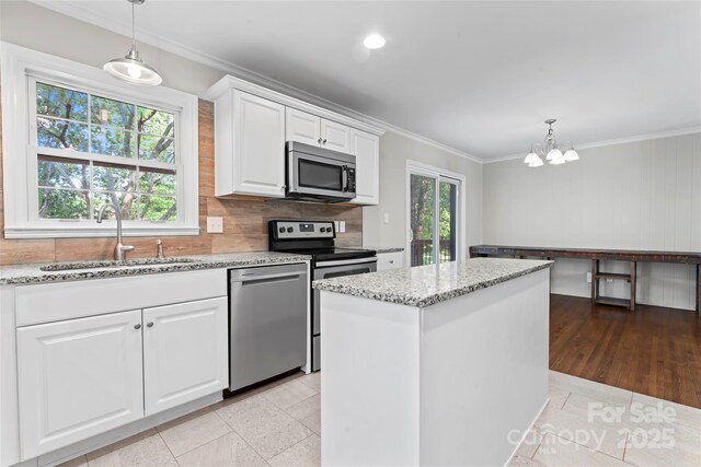 kitchen featuring crown molding, light stone countertops, a chandelier, a sink, and stainless steel appliances