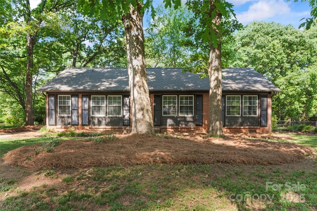 view of front of house featuring brick siding, fence, and roof with shingles