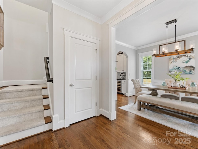 dining space featuring crown molding, arched walkways, baseboards, and dark wood-type flooring