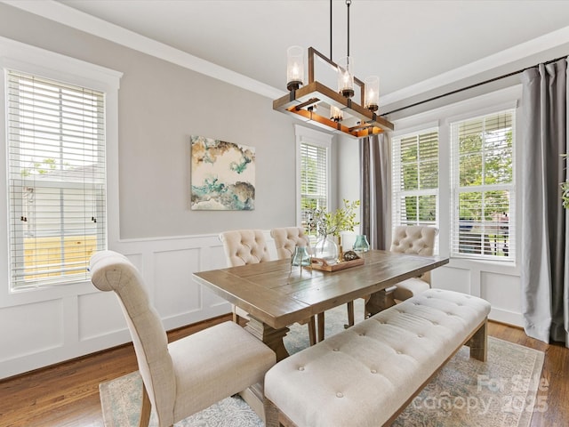 dining area featuring wainscoting, wood finished floors, an inviting chandelier, and a decorative wall
