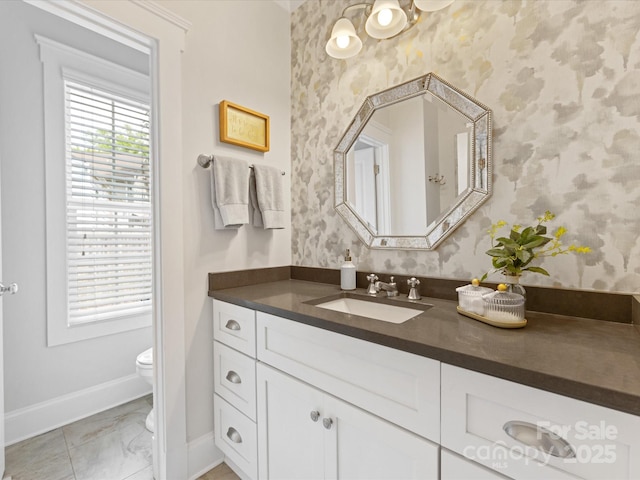 bathroom with vanity, toilet, marble finish floor, baseboards, and wallpapered walls