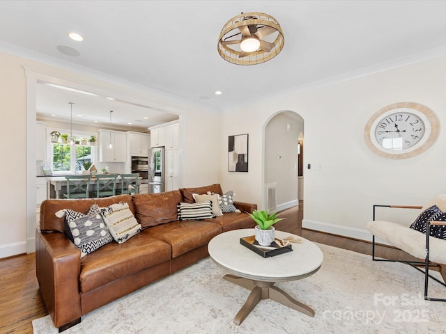 living room with crown molding, visible vents, baseboards, arched walkways, and wood finished floors
