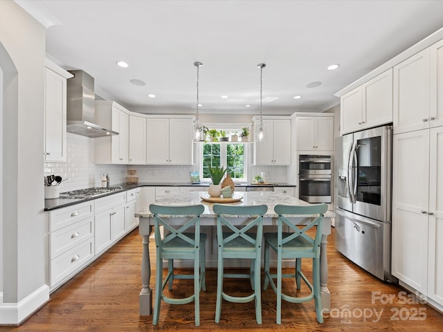 kitchen with tasteful backsplash, wall chimney exhaust hood, appliances with stainless steel finishes, and a kitchen island