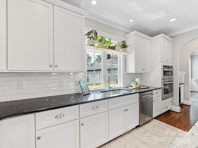 kitchen with recessed lighting, a sink, arched walkways, white cabinets, and appliances with stainless steel finishes