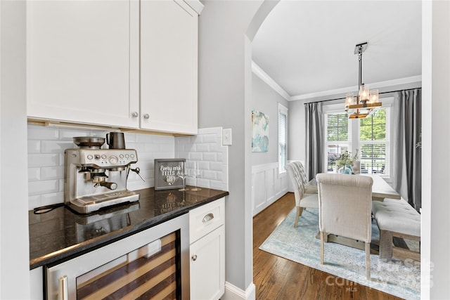 dining area with crown molding, beverage cooler, arched walkways, dark wood-style flooring, and wainscoting