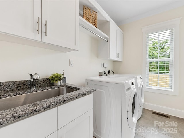 washroom featuring a sink, cabinet space, washer and clothes dryer, visible vents, and baseboards