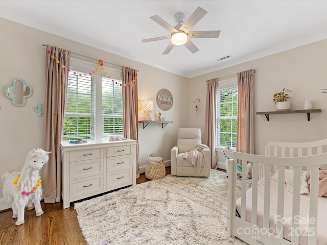 bedroom featuring a crib, ceiling fan, and wood finished floors