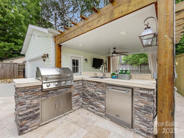 view of patio with grilling area, a sink, fence, ceiling fan, and exterior kitchen