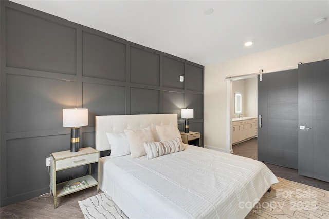 3630 N Davidson St Unit 3301, Charlotte, NC 28205 - bedroom featuring connected bathroom, a barn door, a sink, a decorative wall, and dark wood-type flooring