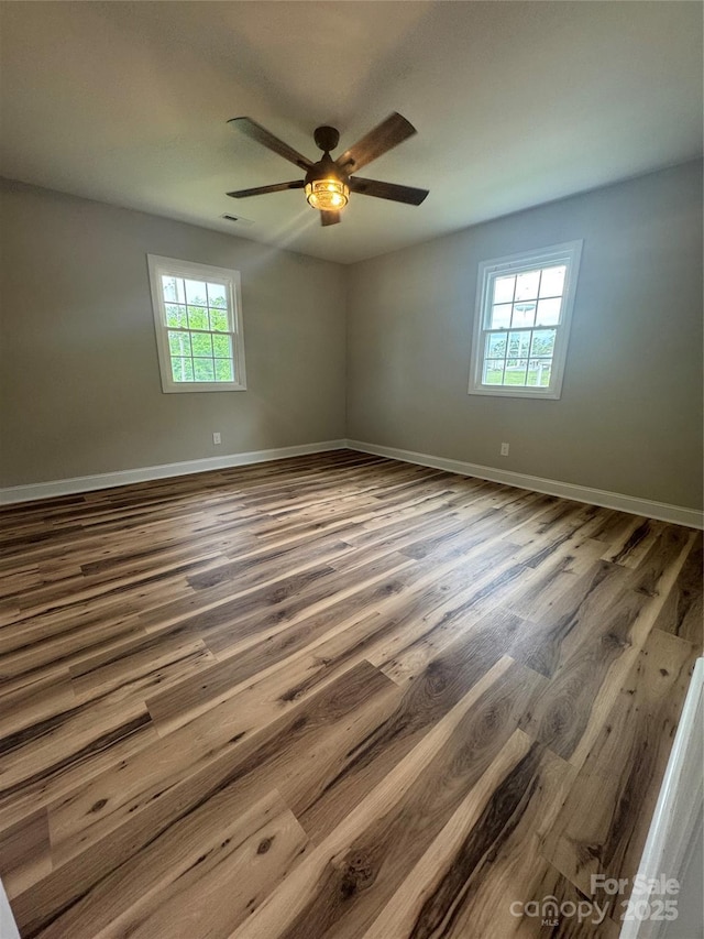 empty room featuring plenty of natural light, baseboards, ceiling fan, and wood finished floors
