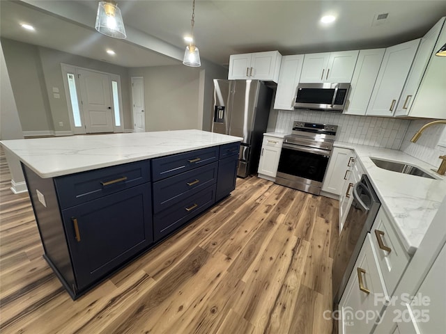 kitchen featuring a kitchen island, appliances with stainless steel finishes, white cabinetry, a sink, and light wood-style flooring