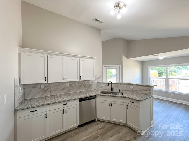 kitchen featuring stainless steel dishwasher, a sink, vaulted ceiling, tasteful backsplash, and light wood-style floors