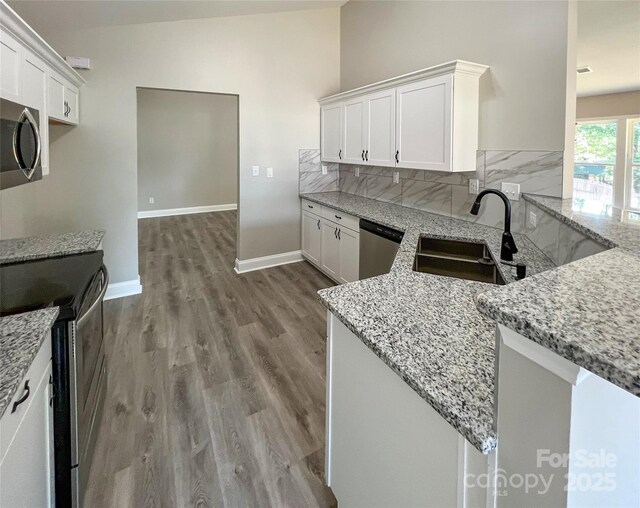 kitchen with stainless steel appliances, a sink, light stone countertops, white cabinets, and dark wood-style flooring