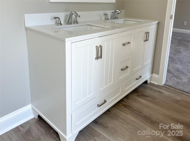 bathroom with wood finished floors, baseboards, and double sink