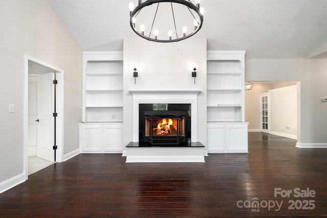 62 Mackenzie Way, Swannanoa, NC 28778 - unfurnished living room with baseboards, a lit fireplace, dark wood-type flooring, built in shelves, and a notable chandelier