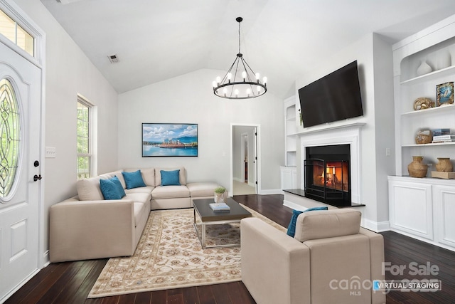 62 Mackenzie Way, Swannanoa, NC 28778 - living room with a warm lit fireplace, an inviting chandelier, built in features, lofted ceiling, and dark wood-style floors