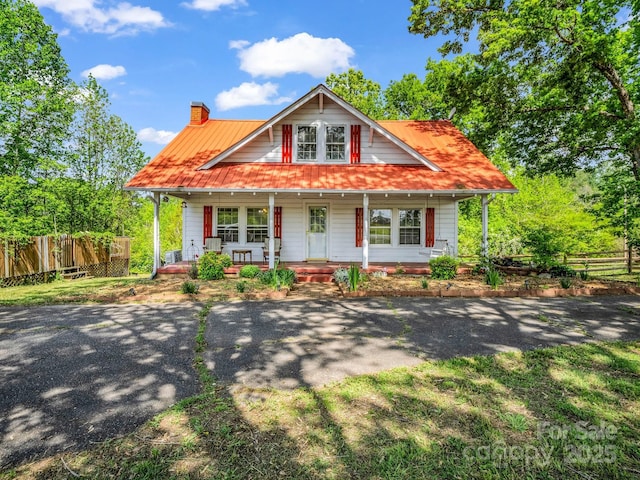 view of front of house featuring fence, covered porch, and a chimney