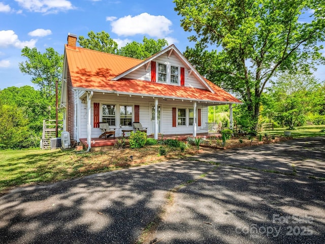 view of front of property featuring covered porch, a chimney, and metal roof