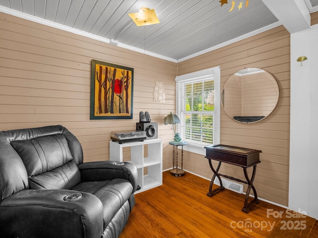 sitting room featuring wood walls, wood ceiling, wood finished floors, and ornamental molding