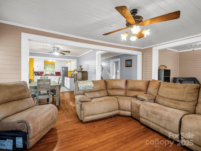 living area with wood finished floors, wooden walls, stairway, wood ceiling, and a ceiling fan