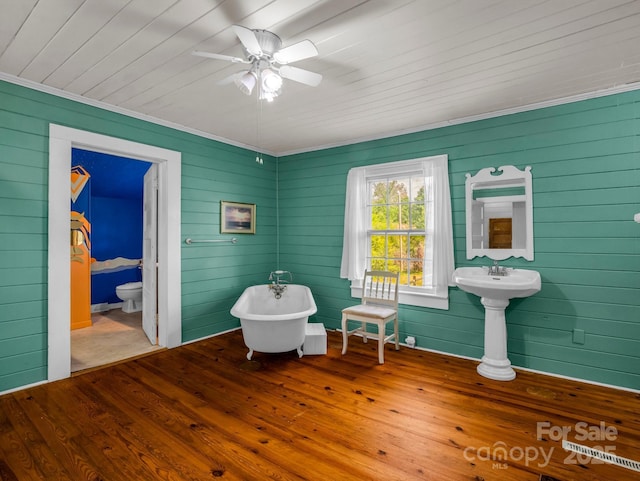 living area featuring wood walls, ornamental molding, wood finished floors, wooden ceiling, and a ceiling fan
