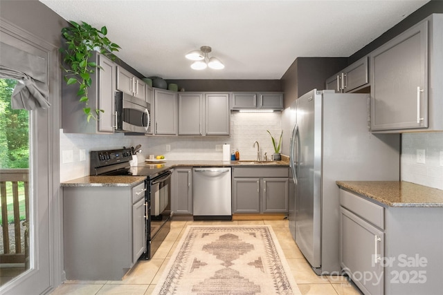 kitchen with decorative backsplash, light tile patterned flooring, gray cabinets, a sink, and appliances with stainless steel finishes