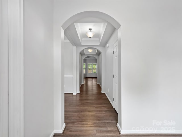 corridor with arched walkways, baseboards, dark wood-type flooring, and a raised ceiling