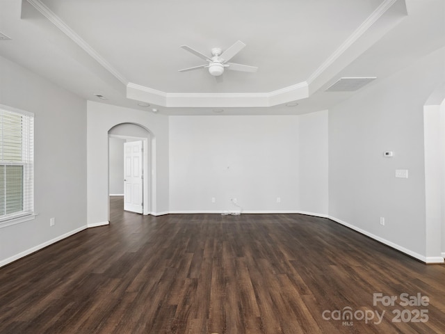 spare room with ceiling fan, arched walkways, ornamental molding, a tray ceiling, and dark wood-type flooring