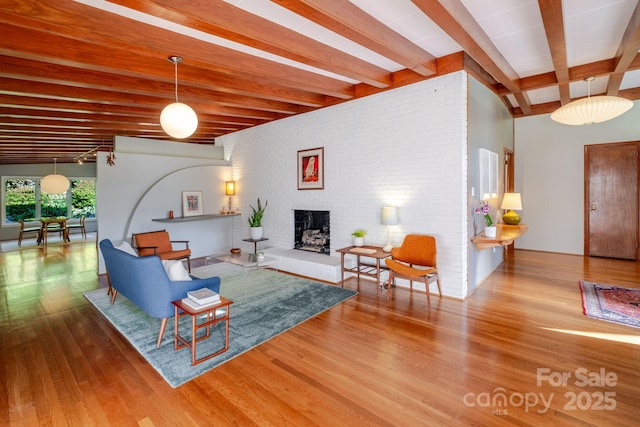 living area with a fireplace, beam ceiling, and wood finished floors