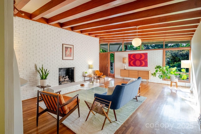 living room with beam ceiling, wood finished floors, brick wall, and a fireplace