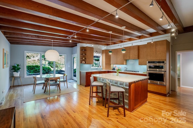 kitchen with brown cabinets, track lighting, light wood finished floors, double oven, and light countertops