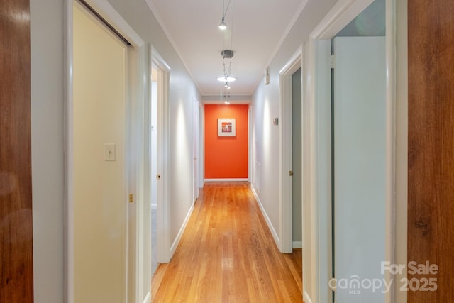 hall with light wood-style floors, ornamental molding, and baseboards