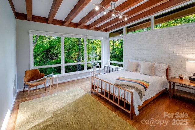 bedroom with wood finished floors, baseboards, beam ceiling, and brick wall